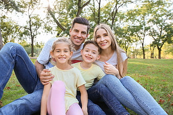 Happy family of four sitting together in a sunny park