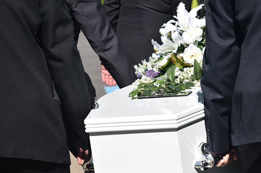 Pallbearers carrying white coffin with flowers at funeral