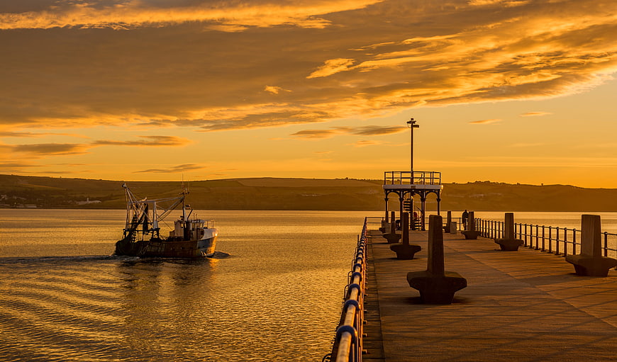 Fishing boat passing pier at golden sunset