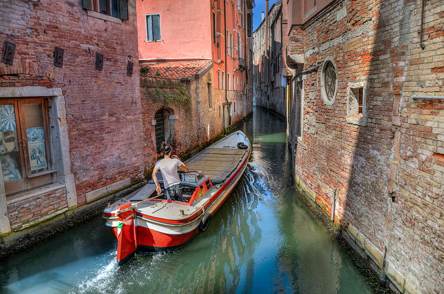 Man steering a boat through a narrow Venice canal