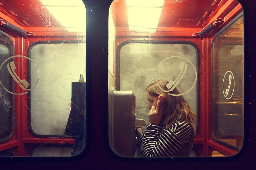 Woman Talking on Phone in Red Telephone Booth
