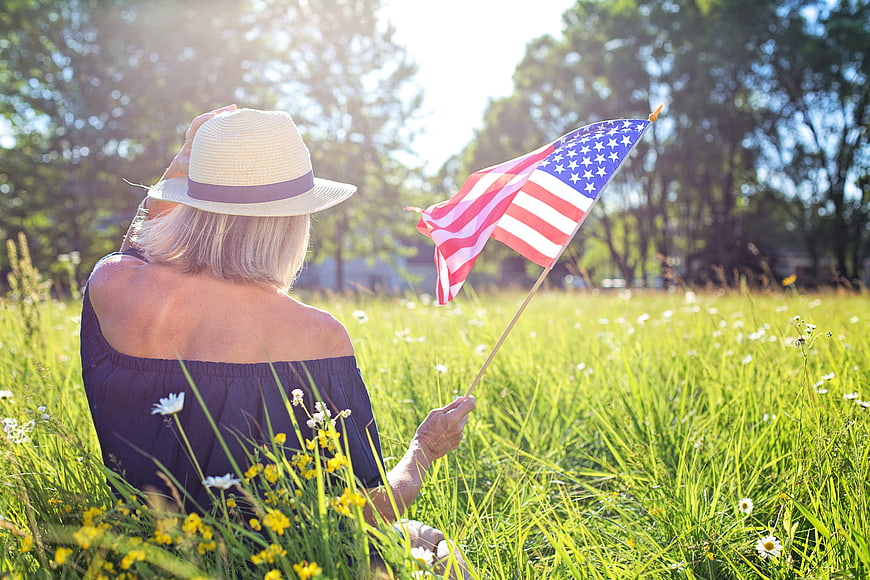Woman with American Flag Sitting in Summer Meadow