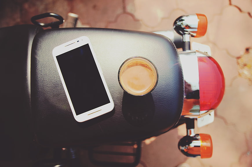 Smartphone and coffee on motorcycle seat top view
