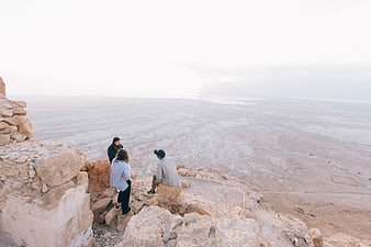 Three friends overlooking vast desert landscape from rocky cliff