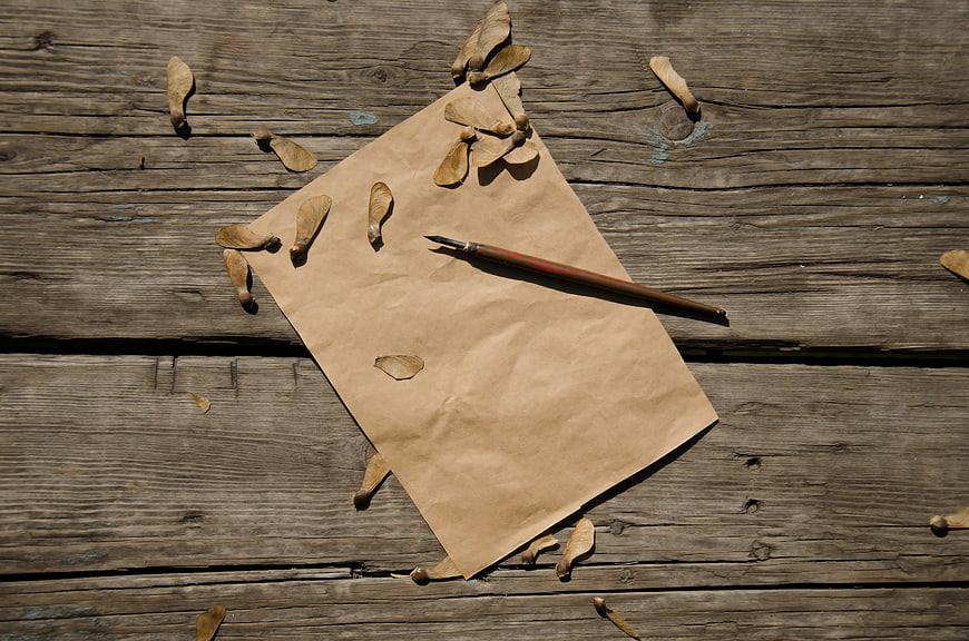 Vintage brown paper and pen on rustic wooden surface with maple seeds