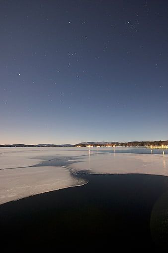 Frozen Lake at Night with Starry Sky and Distant Lights
