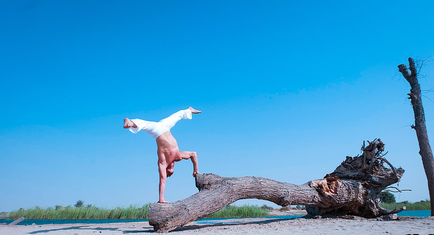 Man performing handstand on driftwood log by blue lake