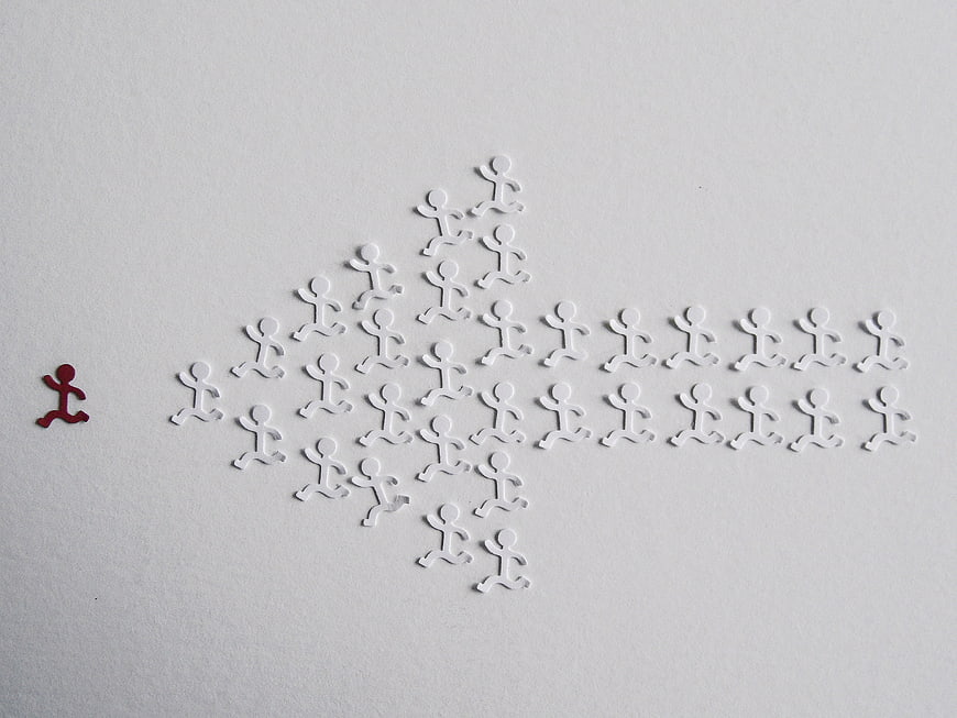 Red figure leading white group in arrow formation on white background