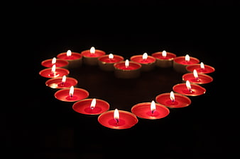 Red tea light candles arranged in a heart shape on black background