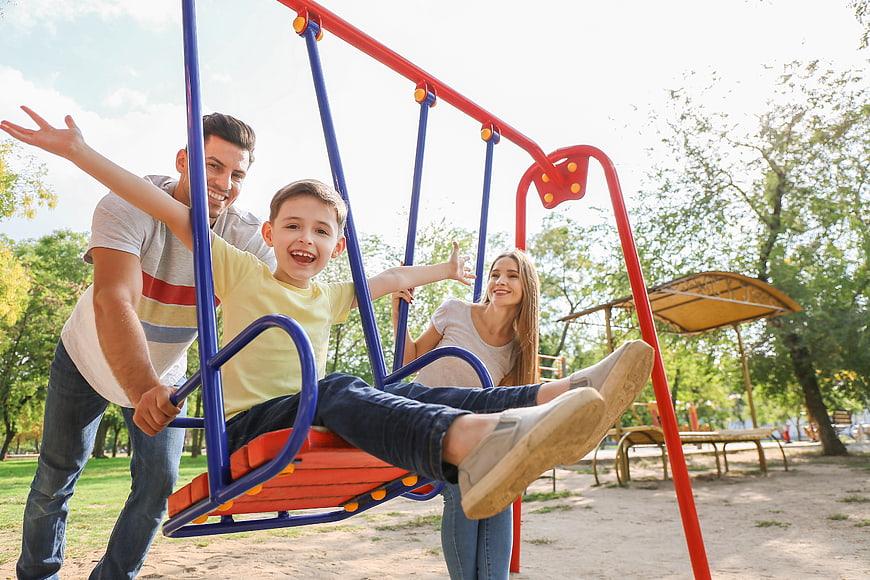 Happy family playing on swings in a sunny park