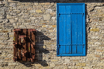 Blue wooden shutters on rustic stone wall with potted plants