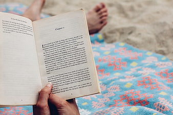 Person reading book on beach towel with bare feet