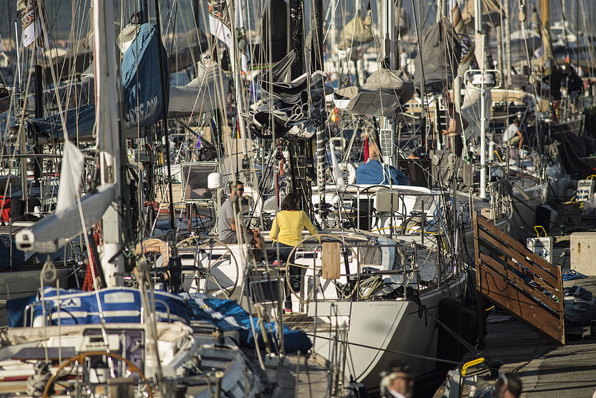 Busy marina with docked sailboats and people preparing for sailing