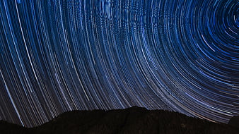 Star trails circling the night sky over a dark mountain silhouette