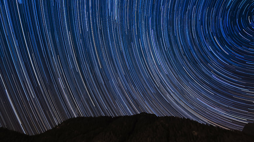 Star trails circling the night sky over a dark mountain silhouette