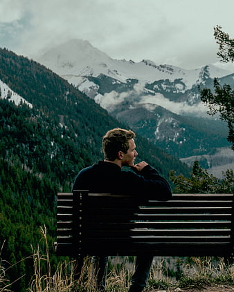 Man sitting on bench overlooking snowy mountain landscape