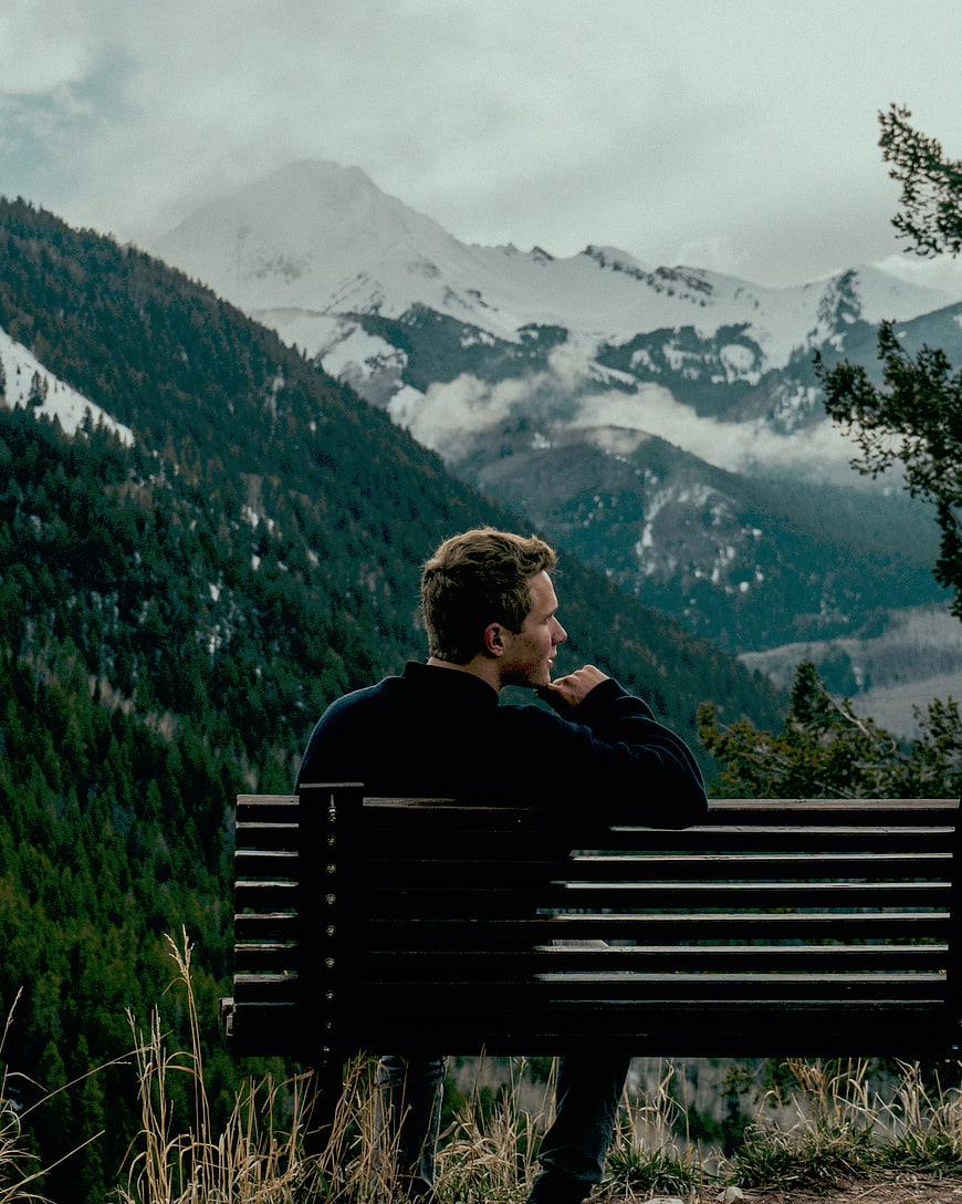 Man sitting on bench overlooking snowy mountain landscape