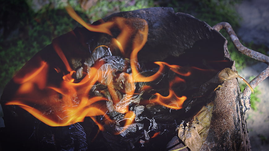 Close-up of burning leaves and charcoal in a rusty metal fire pit