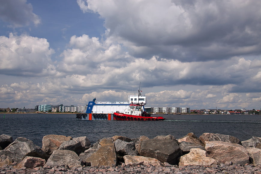 Red tugboat towing barge on cloudy sea with rocks