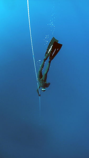 Freediver descending along a rope in deep blue ocean water