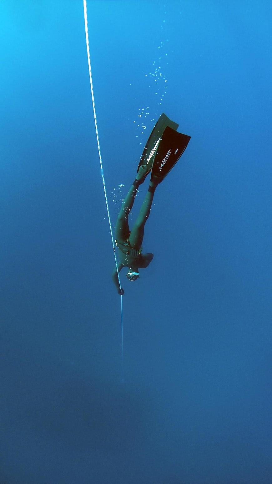 Freediver descending along a rope in deep blue ocean water