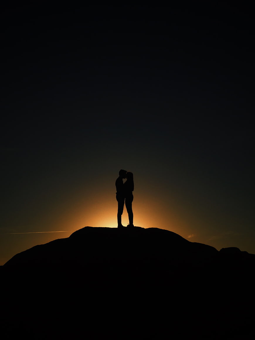 Silhouette of a couple kissing on a mountain peak at sunset