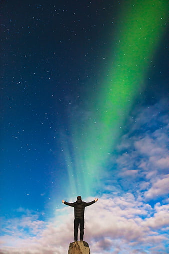 Man with arms raised under green aurora borealis night sky