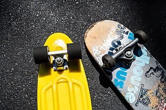 Yellow Penny Board and Worn Skateboard on Asphalt