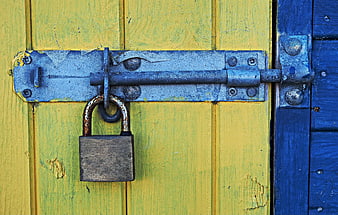 Rusty padlock and blue metal latch on weathered yellow and blue wooden door