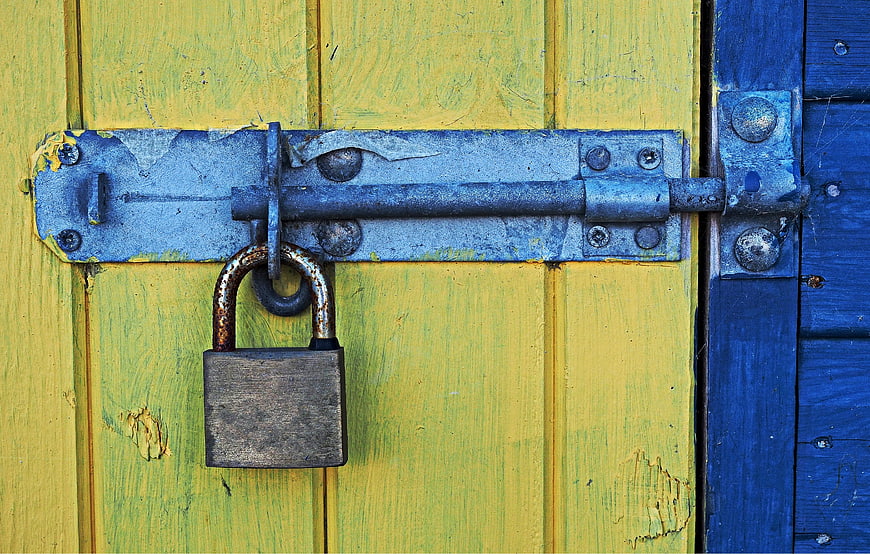 Rusty padlock and blue metal latch on weathered yellow and blue wooden door