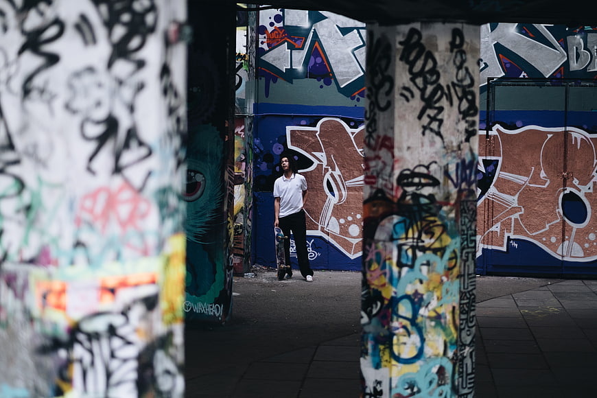 Young man with skateboard in graffiti alley