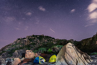 Camping under starry night sky with meteor streak