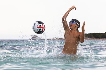 Boy playing water polo in the sea with ball