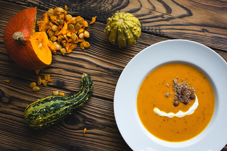 Overhead view of creamy pumpkin soup with roasted seeds and fresh squash on rustic wood
