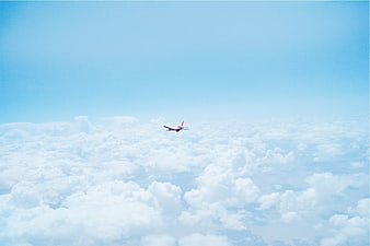 Airplane Flying High Above Fluffy White Clouds in Blue Sky