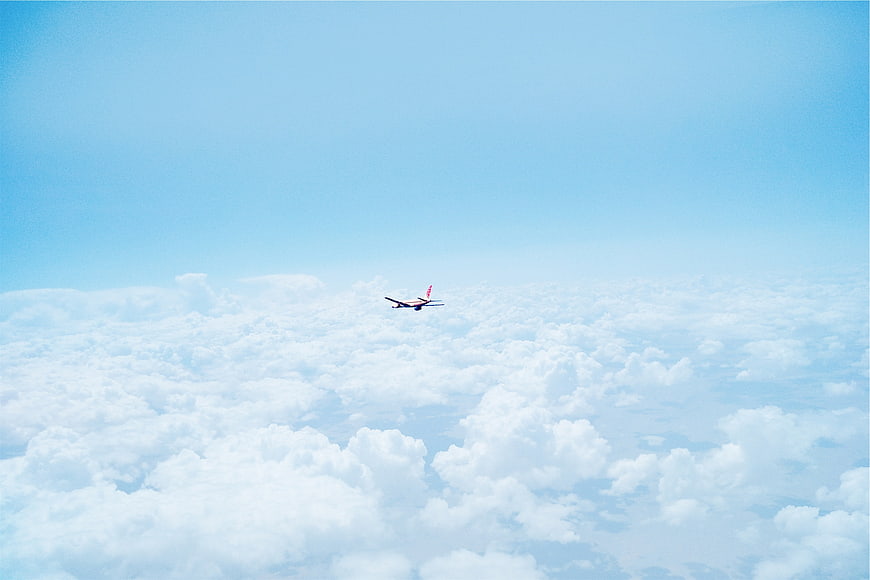 Airplane Flying High Above Fluffy White Clouds in Blue Sky