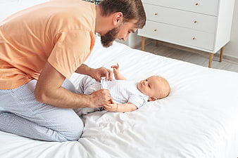 Father Dressing Baby on White Bed