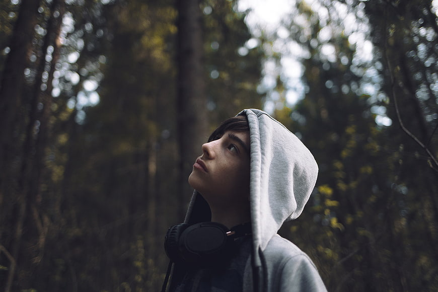 Teenager in Hoodie Looking Up in Forest with Headphones