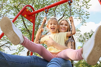 Happy mother and daughter swinging together in a park