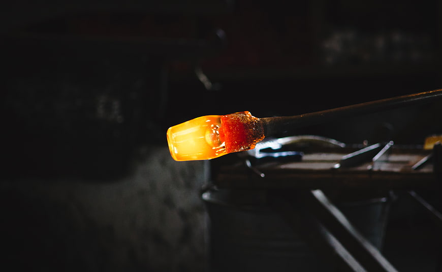 Glowing molten glass on blowpipe in dark workshop