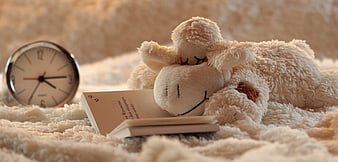 Sleepy stuffed lamb with book and clock on bed