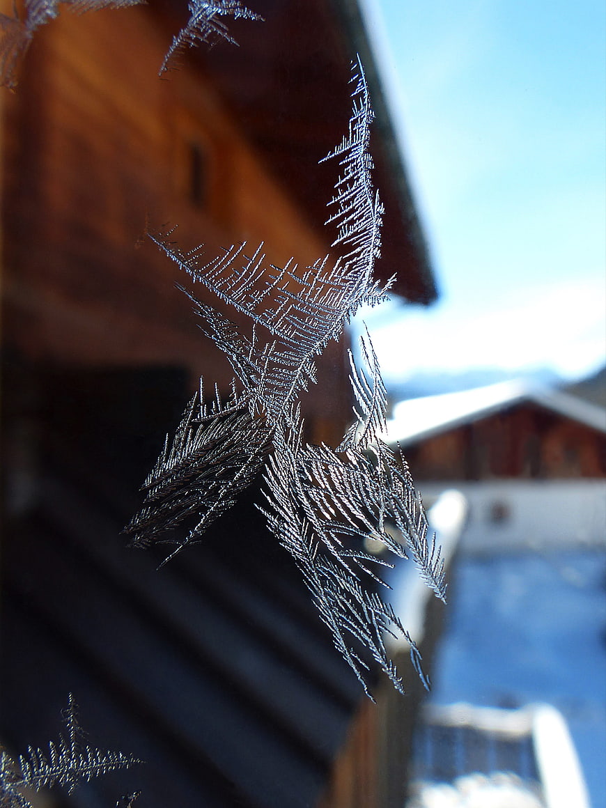 Intricate frost crystals on a window pane with blurred alpine chalet background