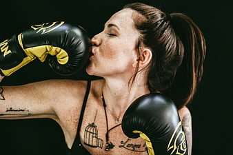Woman kissing boxing glove in black and yellow gear