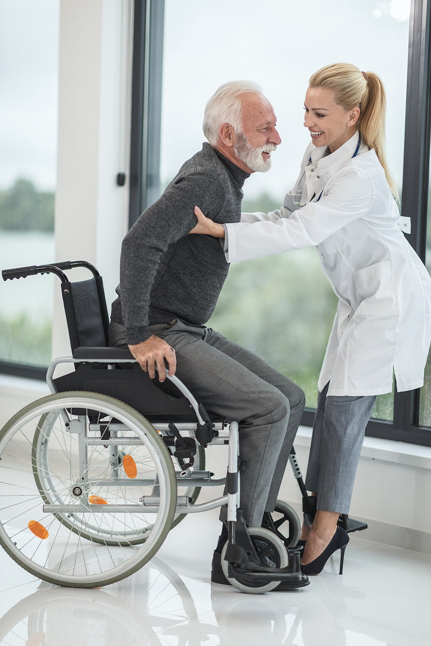 Female doctor helping elderly man in wheelchair stand up