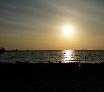 Silhouette of rocky shore with bright sun over ocean horizon