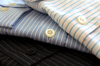 Stack of folded striped dress shirts with close-up buttons
