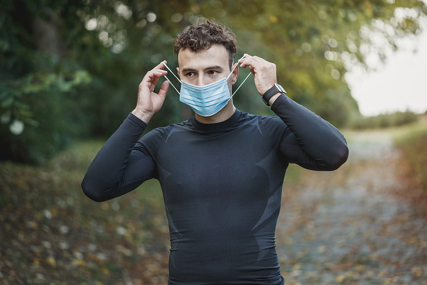 Athletic man putting on face mask outdoors