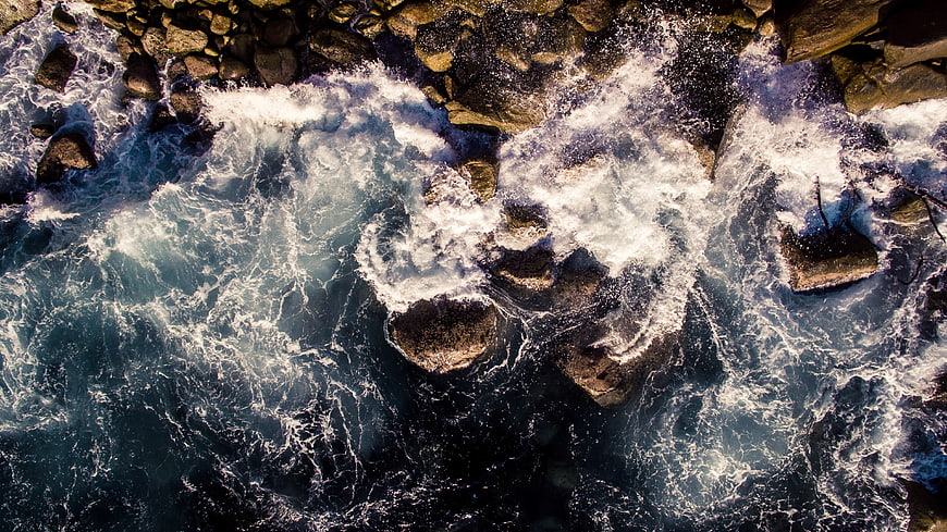Aerial View of Turbulent Ocean Waves Crashing Against Rocky Coastline