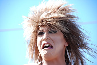 Woman with wild hair screaming intensely against a bright blue sky