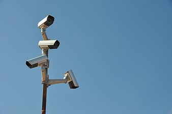 Multiple surveillance cameras mounted on a pole against a clear blue sky